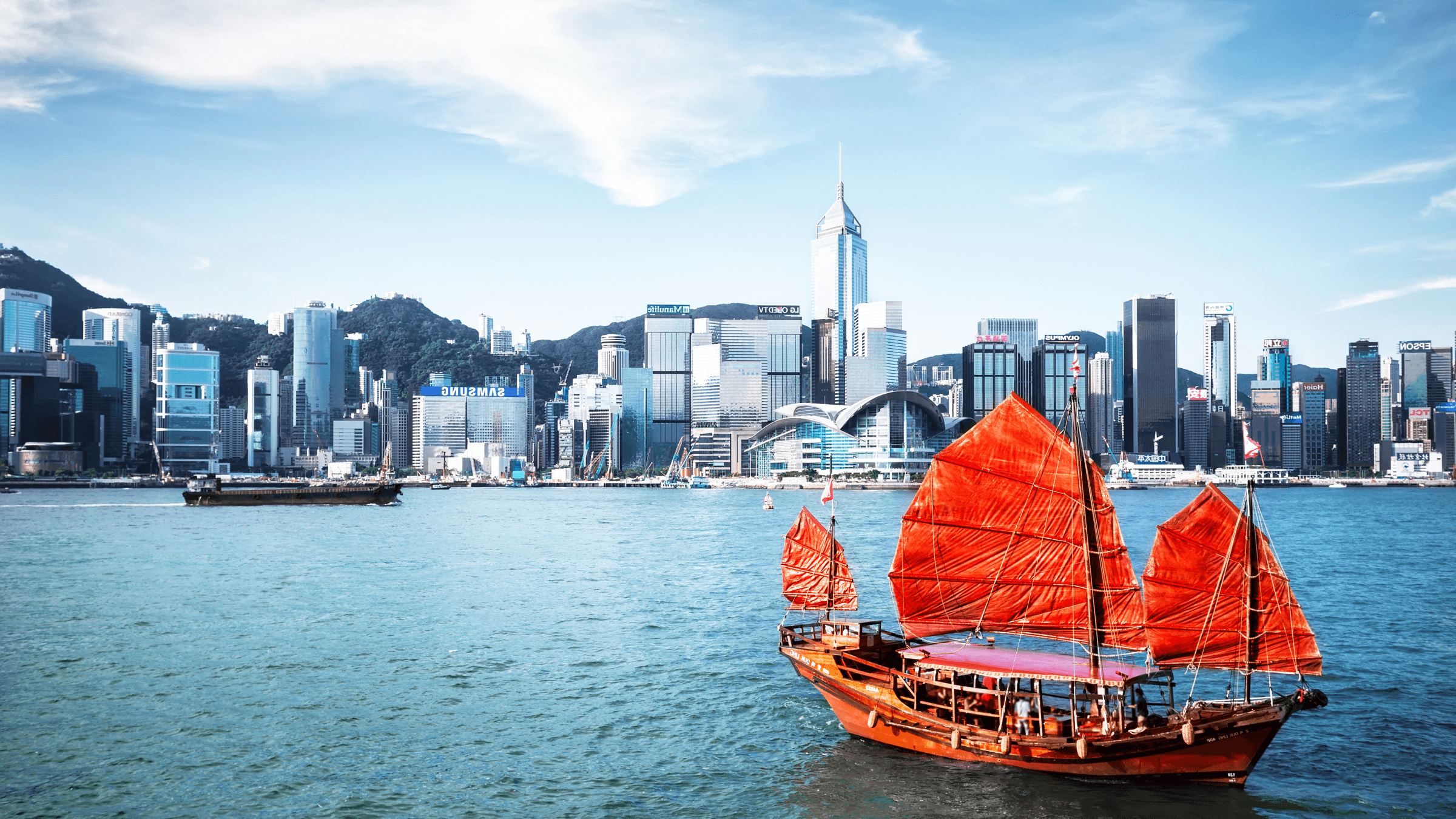 Junk boat sailing in front of the Hong Kong skyline.